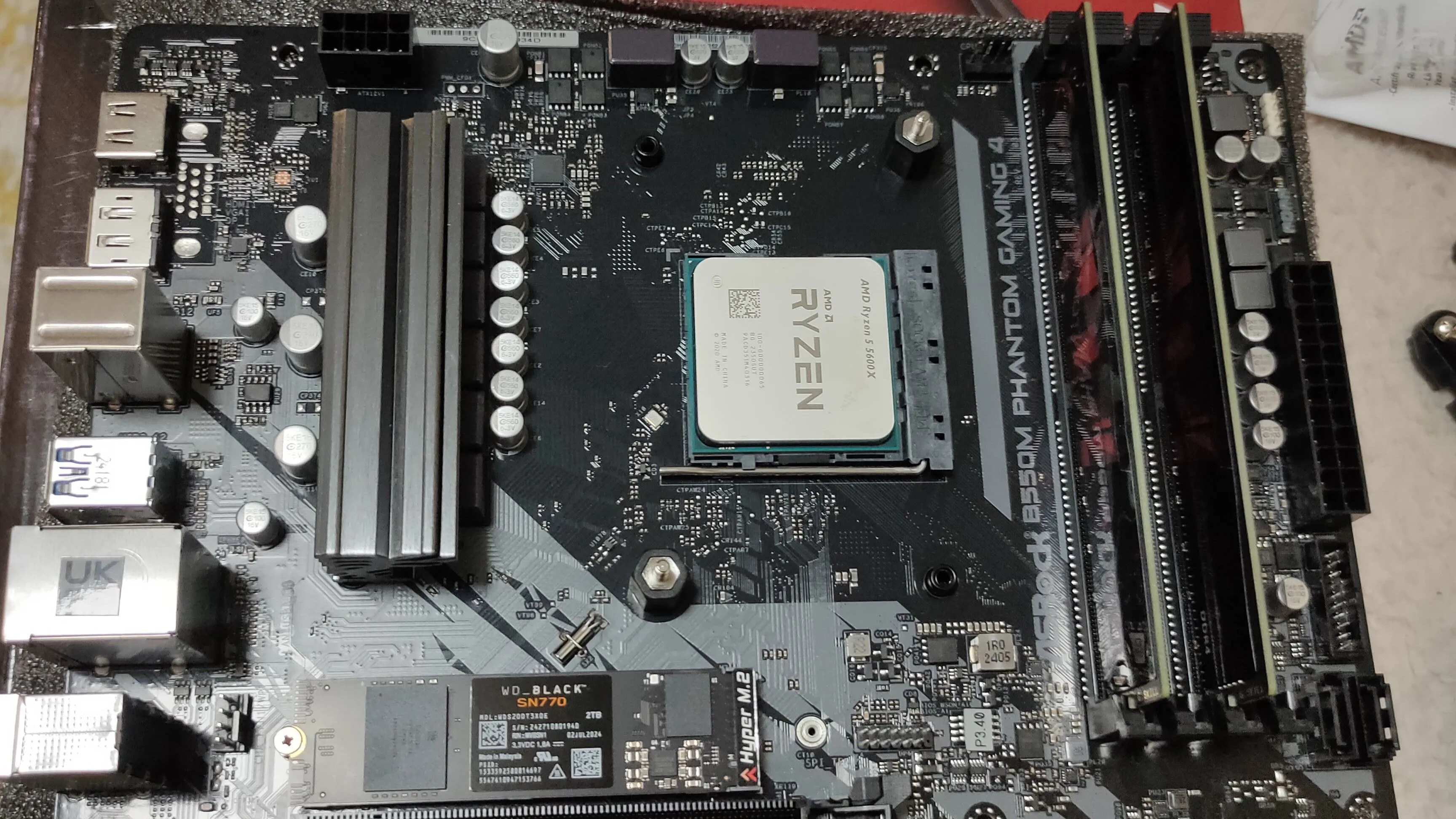 Ảnh cận cảnh một bo mạch chủ B550M cùng CPU Ryzen 5 5600X, RAM DDR4 và SSD NVMe, thể hiện các linh kiện bên trong PC gaming.
