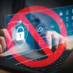 Bàn tay gõ laptop với dấu cấm màu đỏ trên các biểu tượng bảo mật, biểu thị hạn chế truy cập kỹ thuật số.