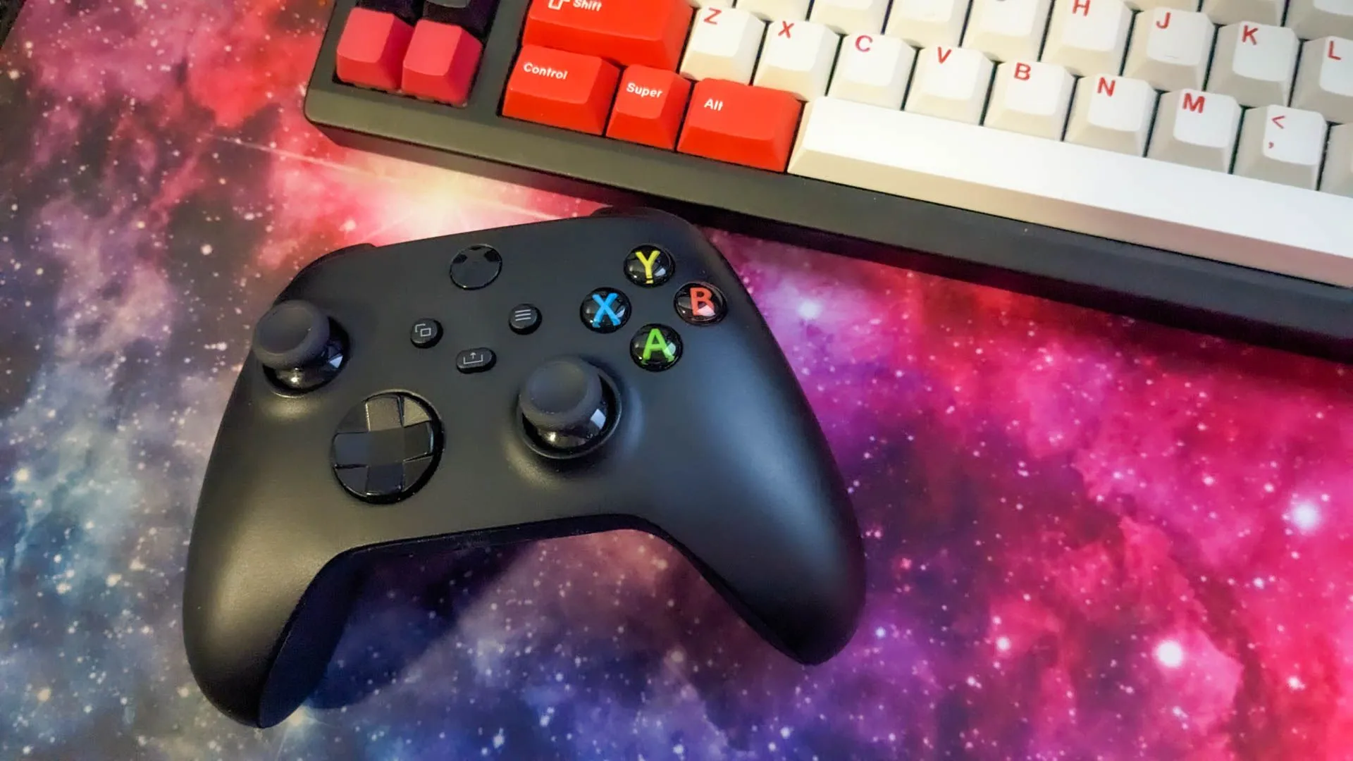 Bộ điều khiển Xbox bên cạnh bàn phím cơ trên tấm lót chuột hình không gian