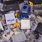 Bộ sưu tập đa dạng các hệ máy chơi game retro, tay cầm và băng đĩa game được chụp từ trên cao, tượng trưng cho kỷ nguyên TV CRT.