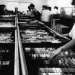 Các nhân viên đang sắp xếp những xấp thẻ đục lỗ của hệ thống máy tính IBM, minh họa phương pháp lưu trữ dữ liệu sơ khai.