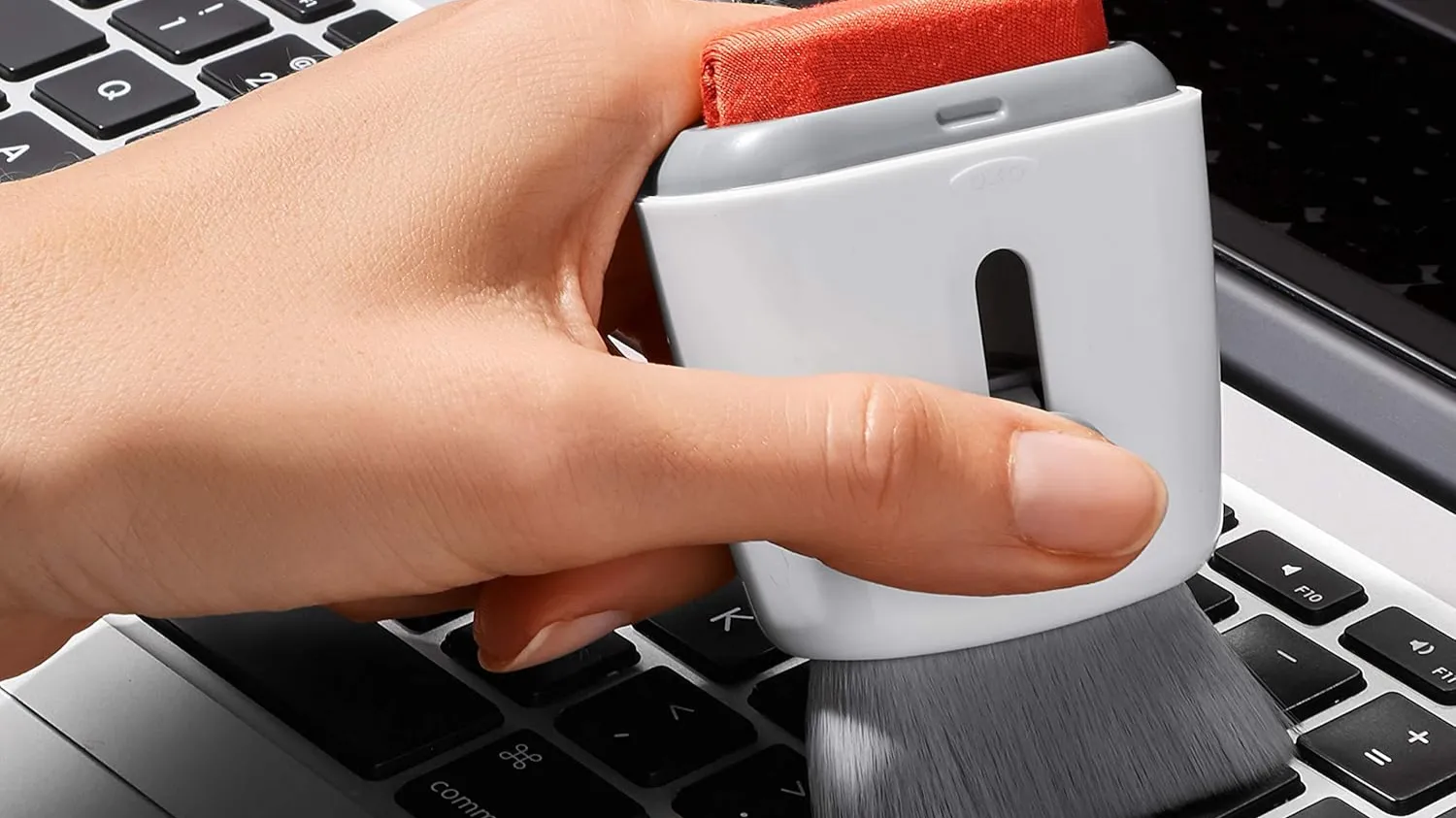 Cọ vệ sinh OXO Good Grips Sweep &amp; Swipe đang được sử dụng để làm sạch bụi bẩn trên bàn phím laptop.