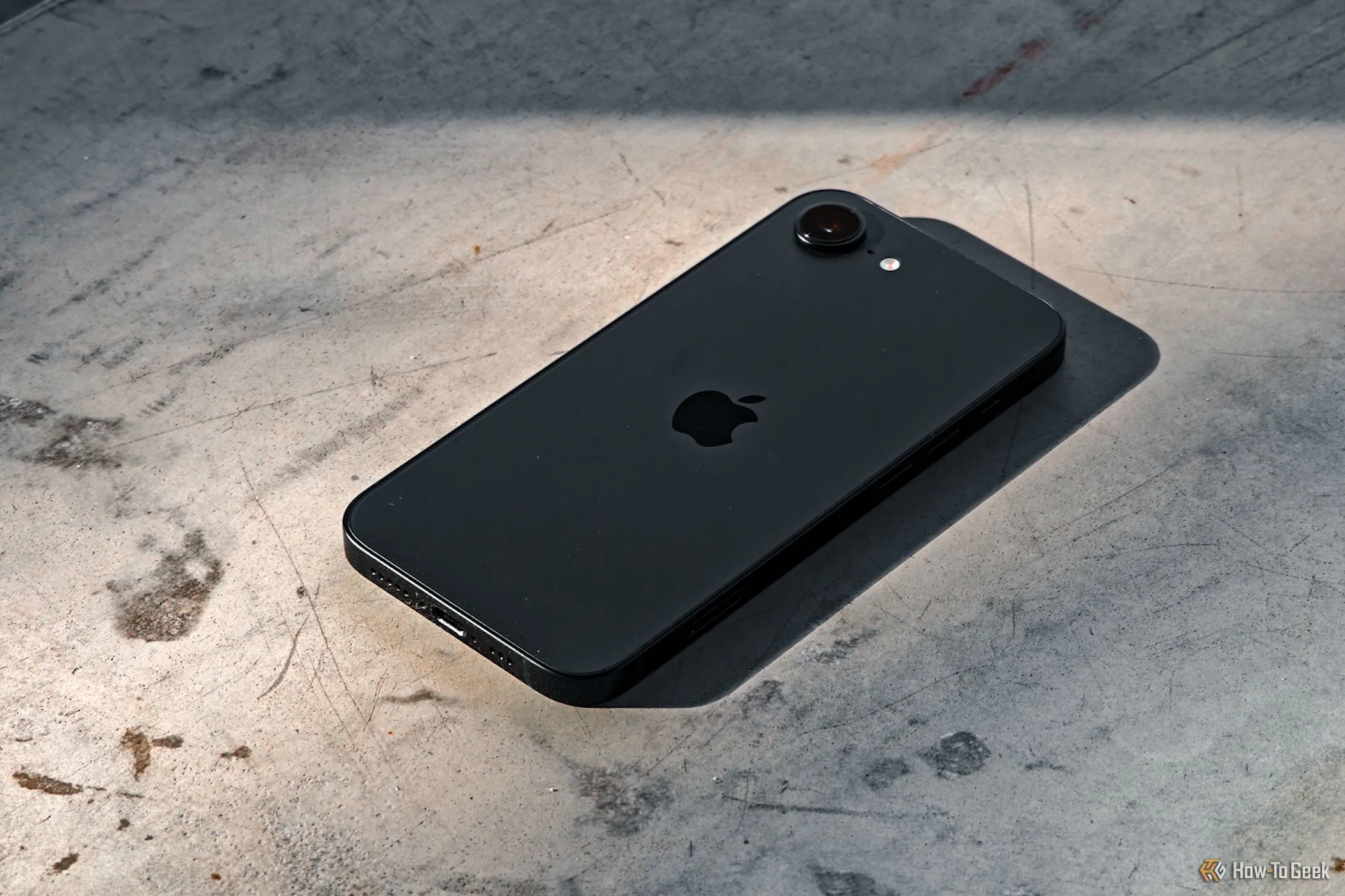 Điện thoại iPhone 16e màu đen với mặt lưng hướng lên trên, đặt trên nền bê tông