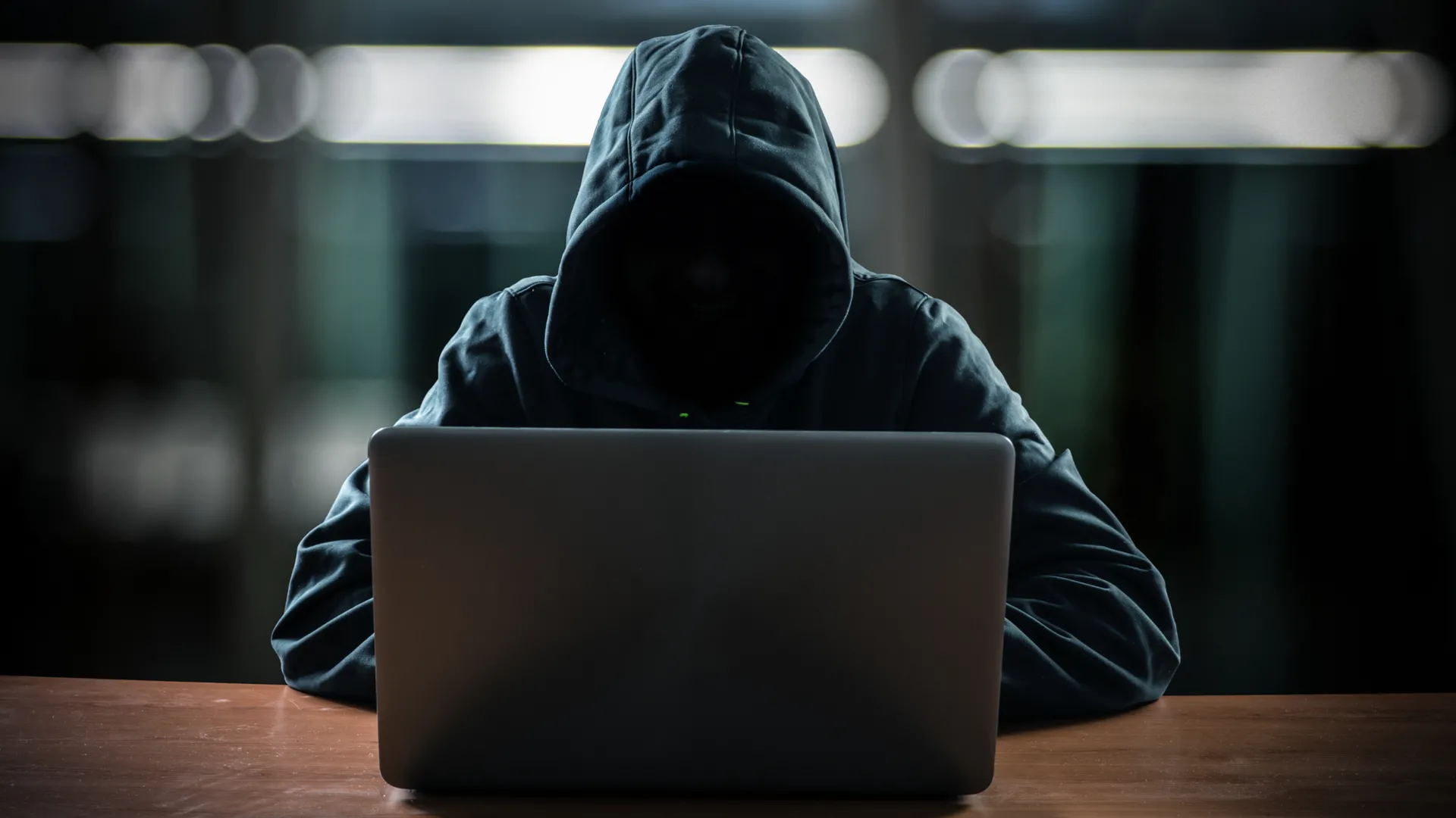 Hacker với khuôn mặt tối, ngồi trước máy tính, thể hiện nguy cơ an ninh mạng và rủi ro tấn công qua cổng dữ liệu trên điện thoại.