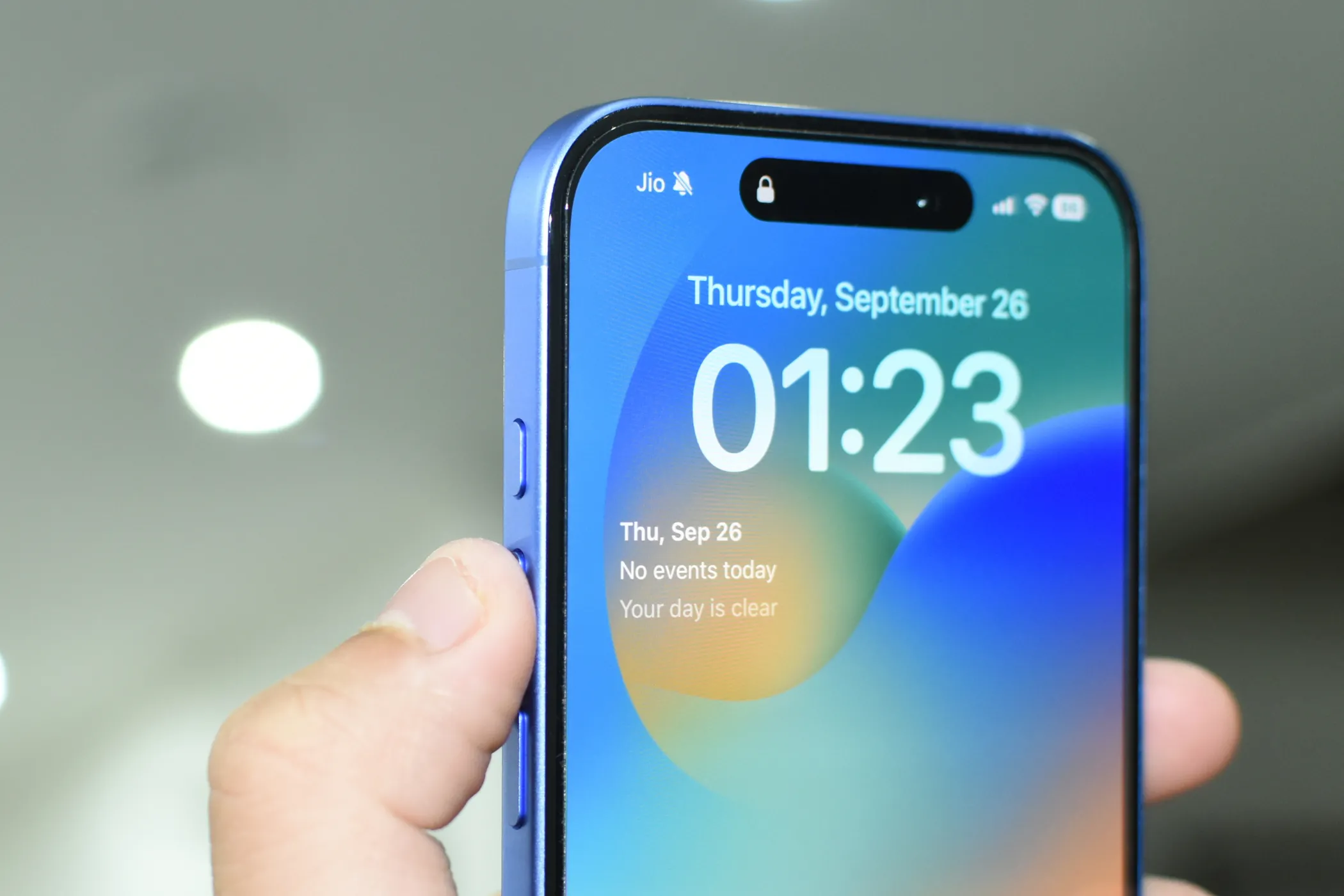 iPhone 16 màu xanh Ultramarine với ngón tay cái chỉ vào nút Tác Vụ ở cạnh trái.