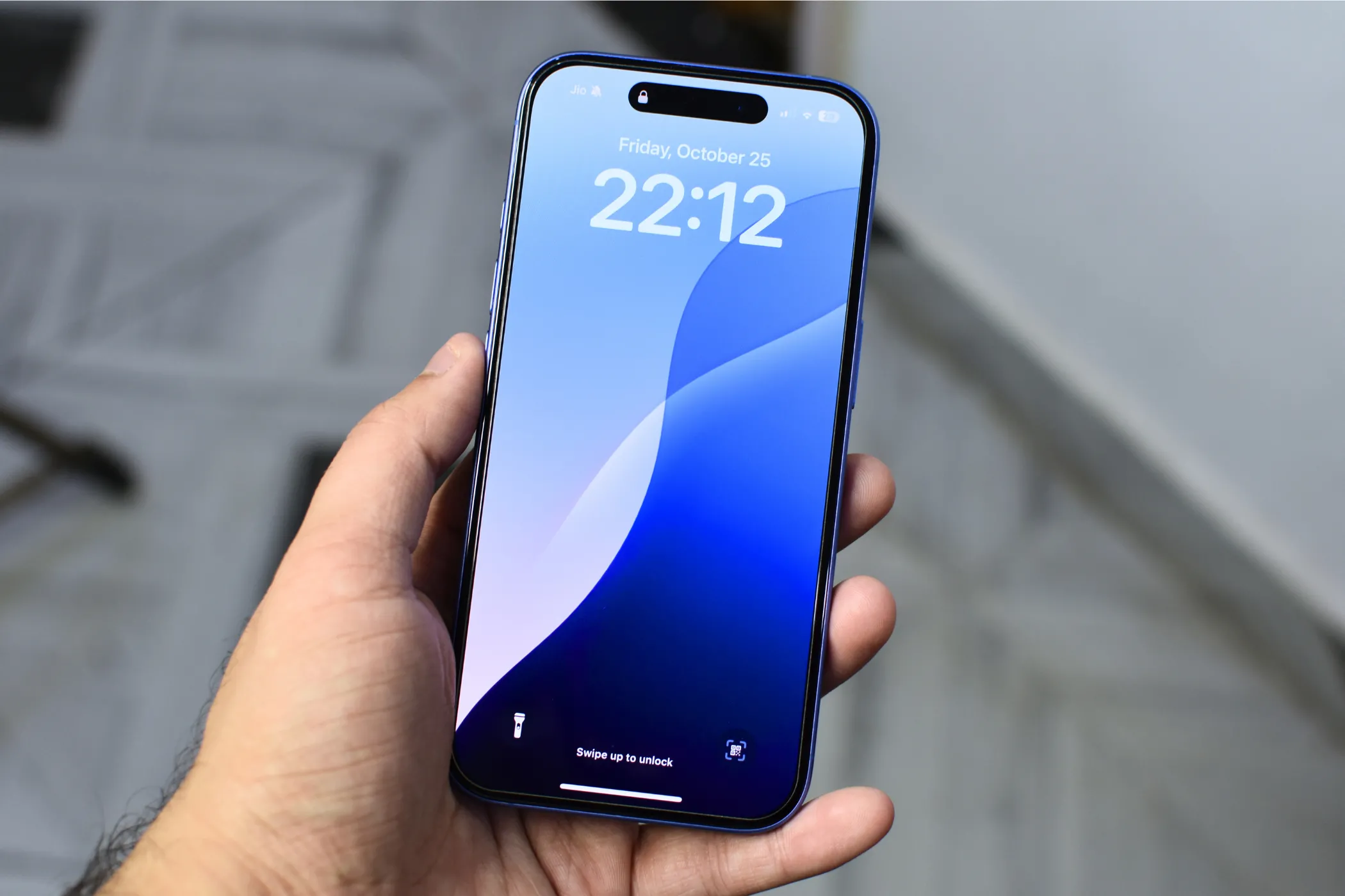 iPhone 16 Plus đang được cầm trên tay với màn hình hiển thị hình nền khóa màu xanh dương.