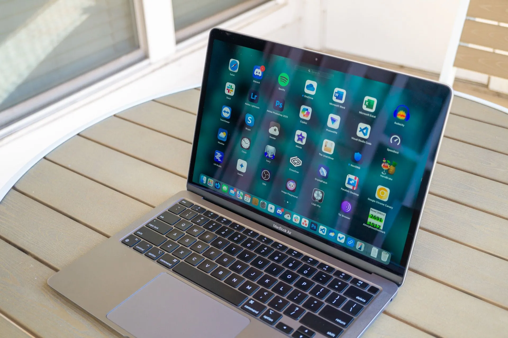 Laptop Apple MacBook Air M1 (2020) với giao diện Launchpad, đặt trên bàn ngoài trời.