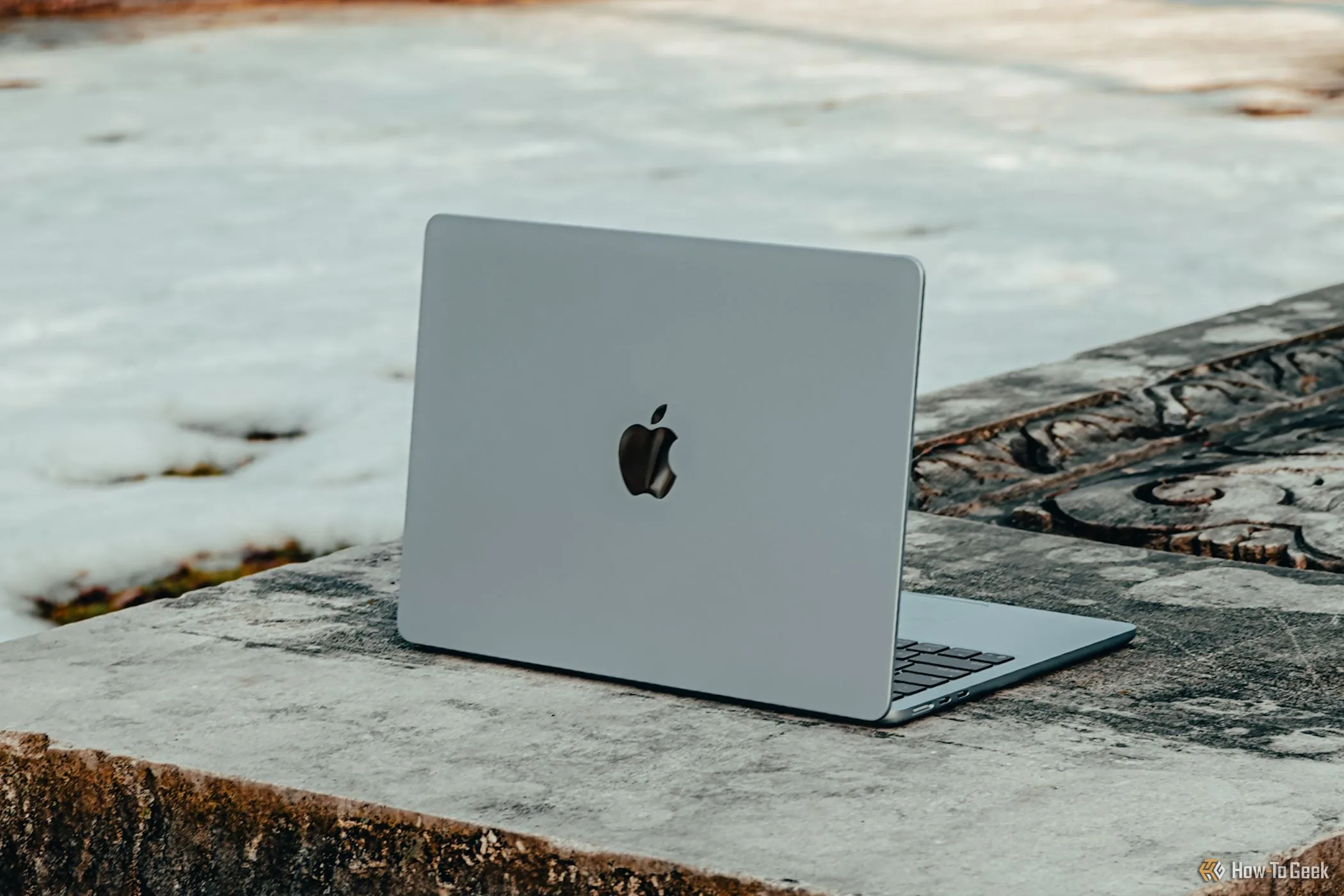 Laptop MacBook Air M4 màu xanh da trời đặt nghiêng trên ghế đá bê tông, thể hiện thiết kế mỏng nhẹ và hiệu năng cao.