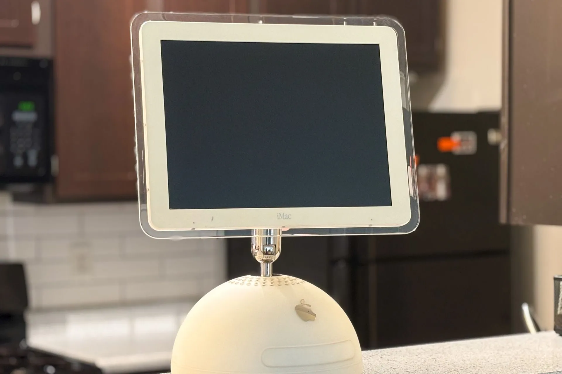 Máy tính Apple iMac G4 với thiết kế độc đáo, màn hình phẳng xoay, đặt trên mặt bàn bếp.