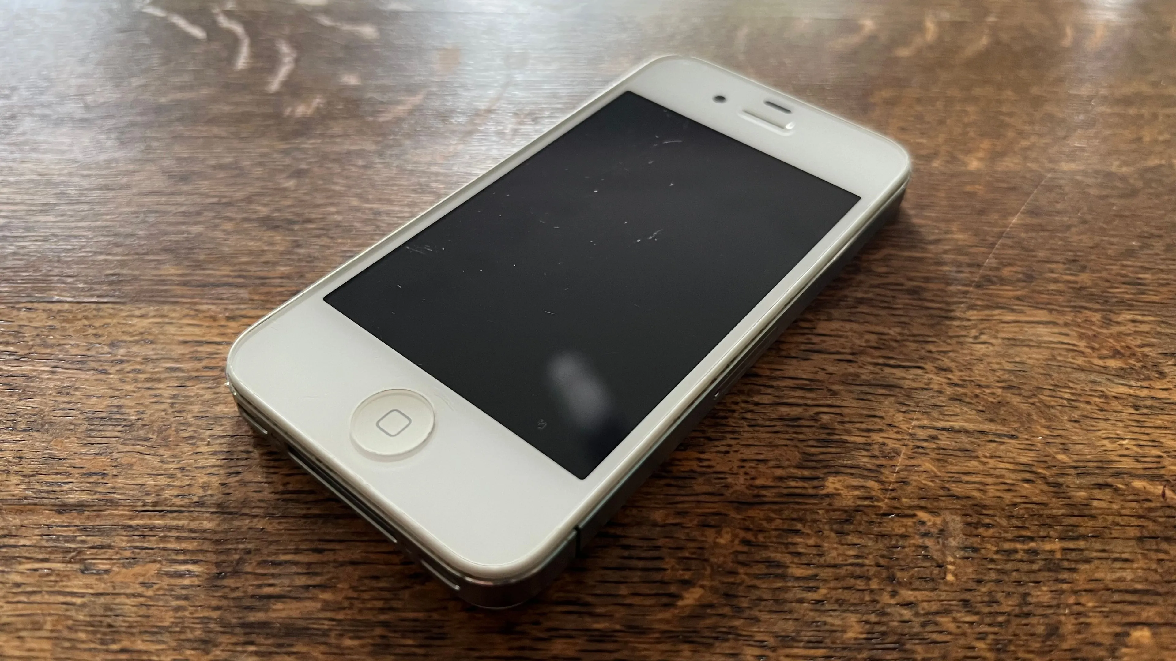 Một chiếc iPhone 4S màu trắng được đặt trên nền màu xám, đại diện cho những thế hệ điện thoại cũ cần được xử lý hoặc tái chế đúng cách.