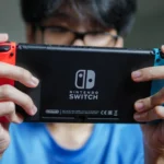 Một người đàn ông đang chơi Nintendo Switch ở chế độ cầm tay, thể hiện sự không thoải mái.
