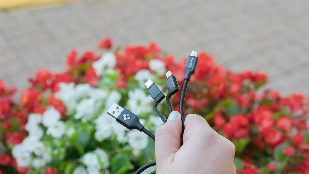 Người dùng đang cầm cáp sạc đa năng Spigen DuraSync 3-in-1 với các đầu nối Lightning, Micro-USB và USB-C.