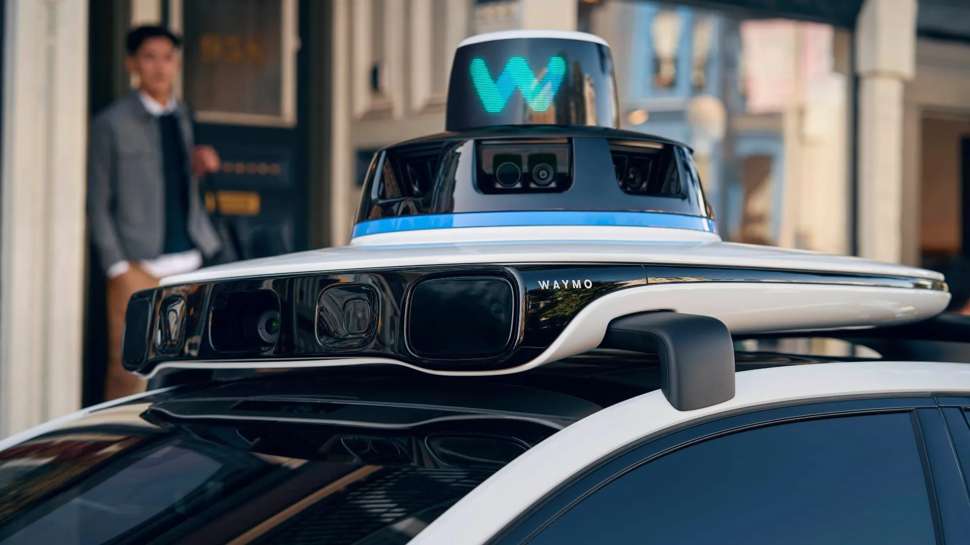 Xe taxi tự lái Waymo Jaguar I-Pace với các cảm biến và thiết bị lidar trên nóc xe, đang di chuyển trên đường phố.